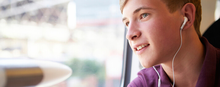Junger Mann mit Kopfhören im Ohr schaut aus dem Zugfenster.